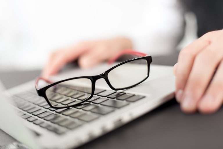 glasses on top of the laptop with person hand