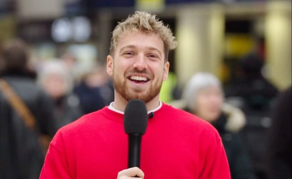 Sam Thompson holding a mic and smiling